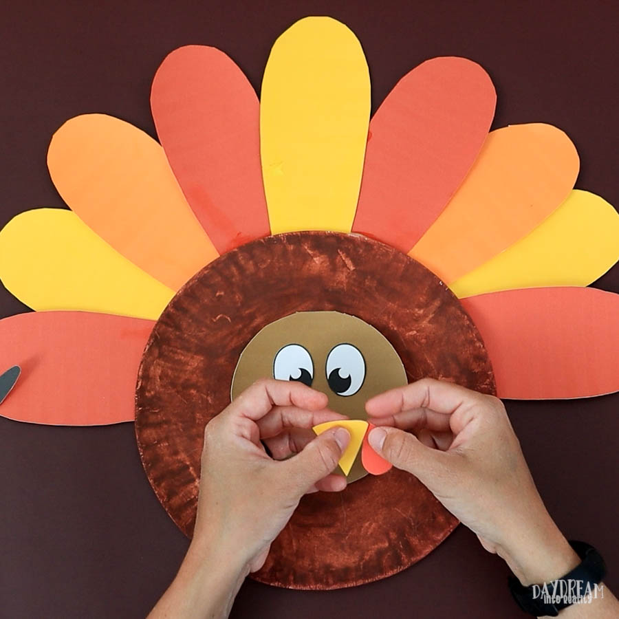 glue beak and and beak and snood on paper plate turkey craft.